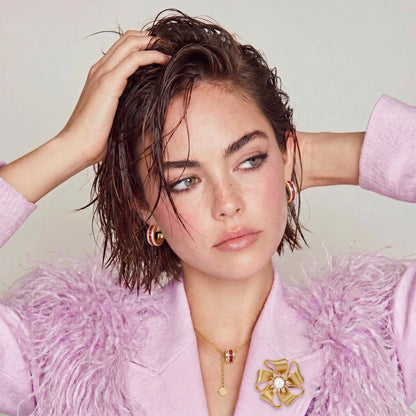 Gold Bloom flower brooch worn on a pale pink top beneath a fluffy purple jacket.