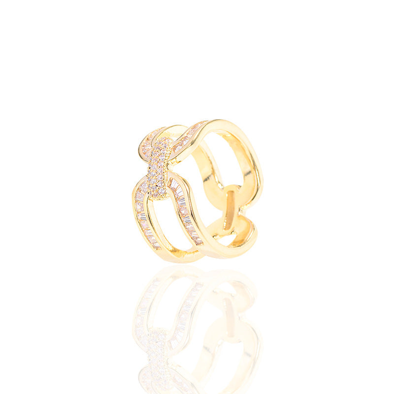 Gold-tone scarf ring with interlocking loops and a reflection on a white surface.