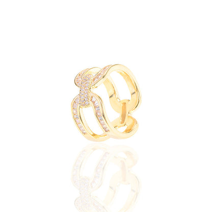 Gold-tone scarf ring with interlocking loops and a reflection on a white surface.