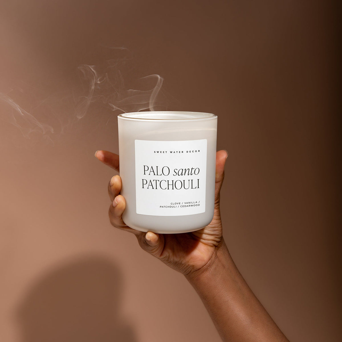 Palo Santo Patchouli candle in a tan jar held against a warm brown background.