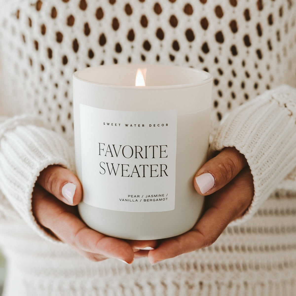 Lit Favorite Sweater candle held in both hands by a person wearing a cream knit sweater.