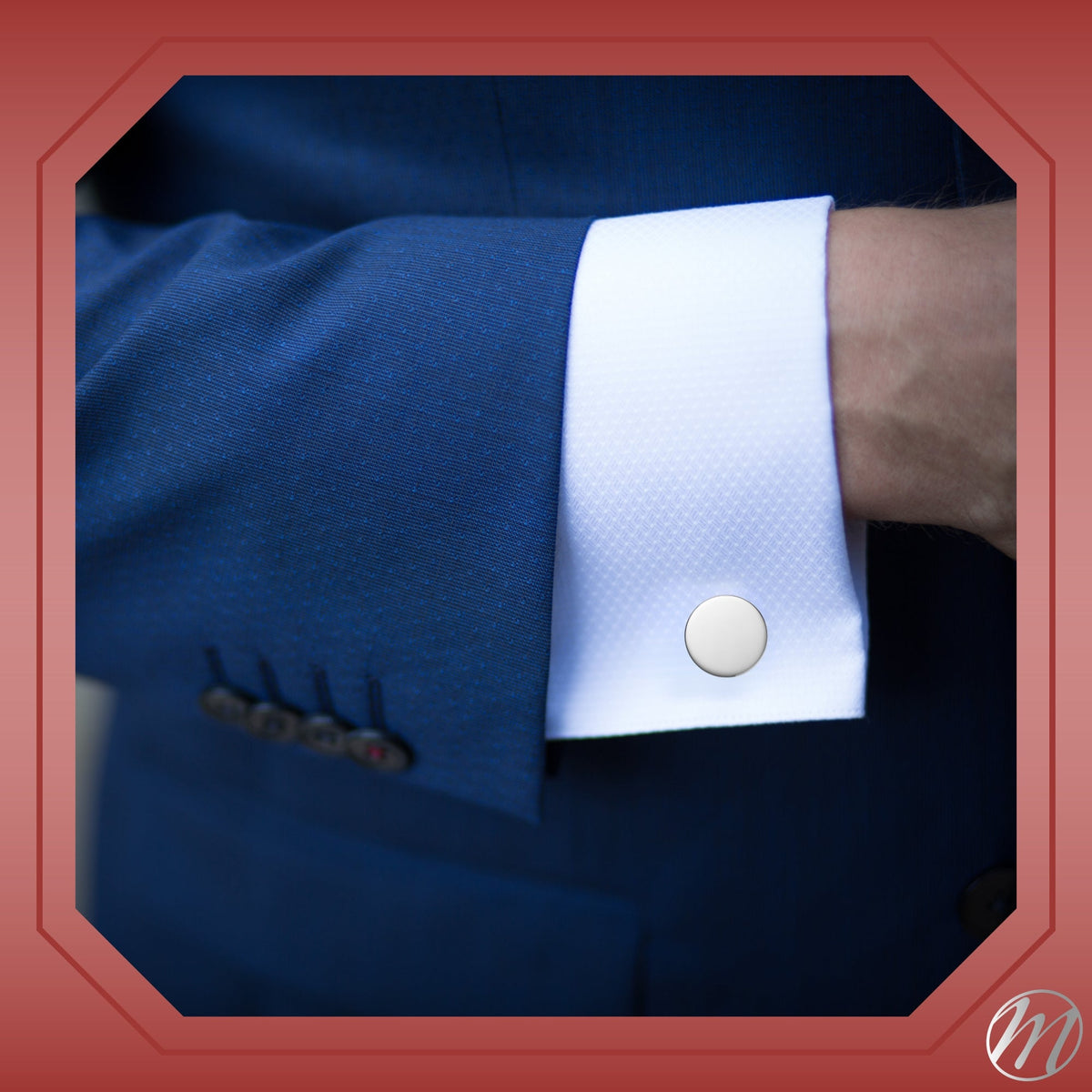 Round sterling silver cufflink on a white French cuff beneath a blue suit sleeve.