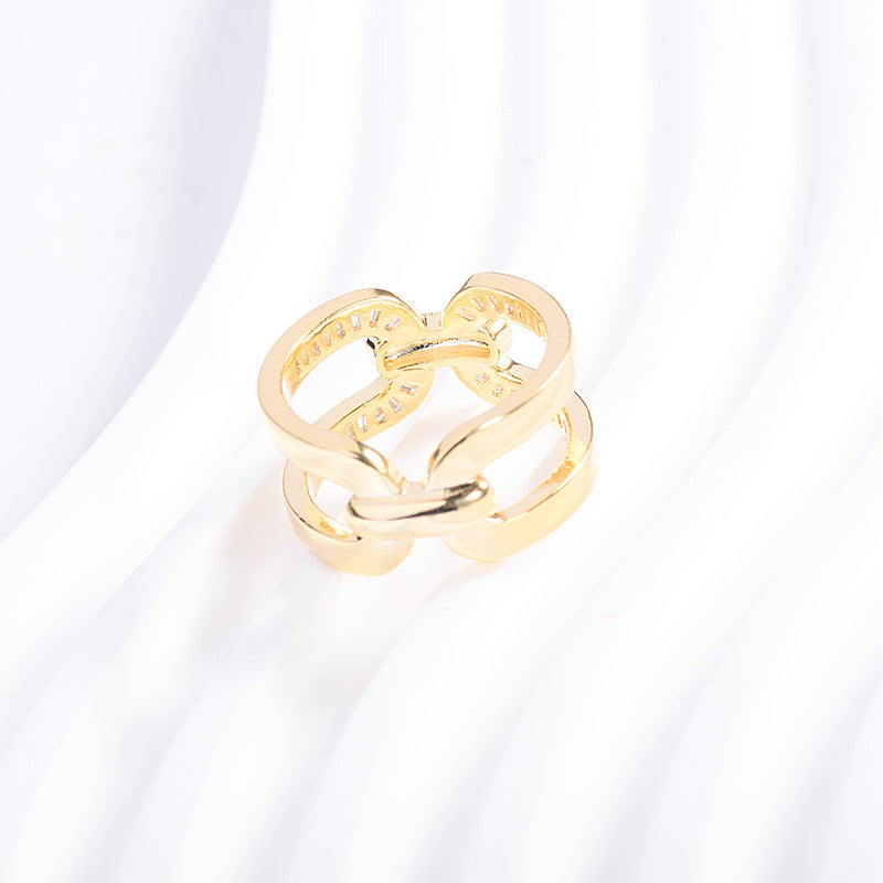 Angled view of a gold-tone scarf ring with interlocking loops on white folded fabric.